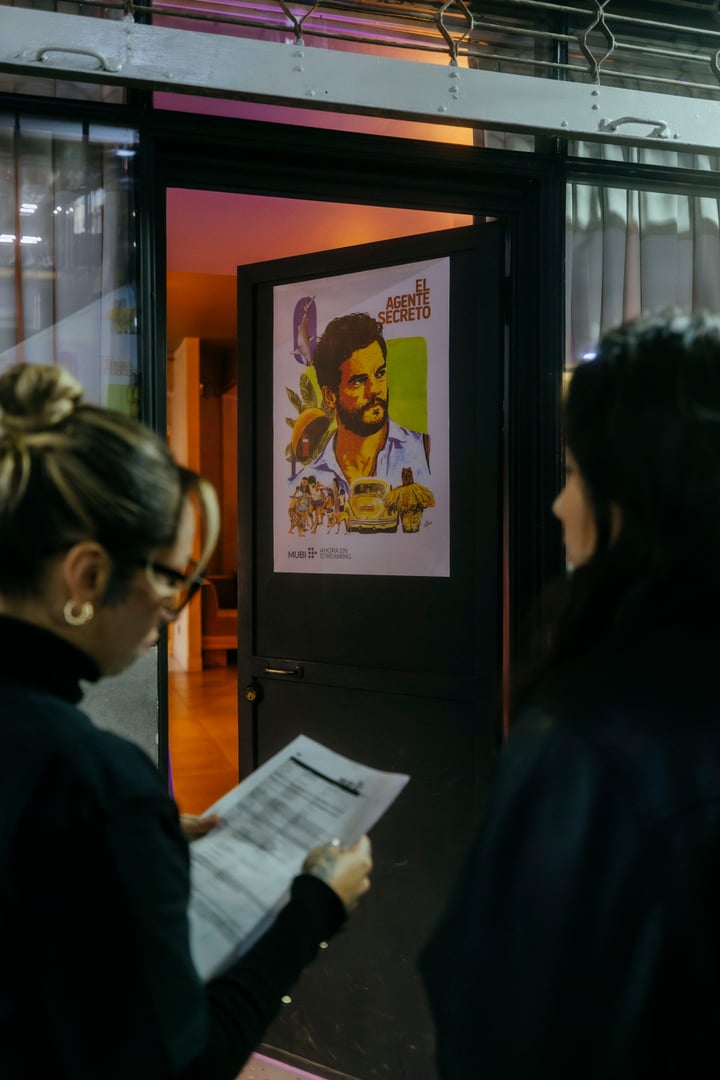 Invitadas observando el afiche de El Agente Secreto en la entrada