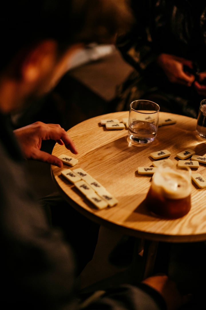 Manos jugando dominó sobre una mesa del bar