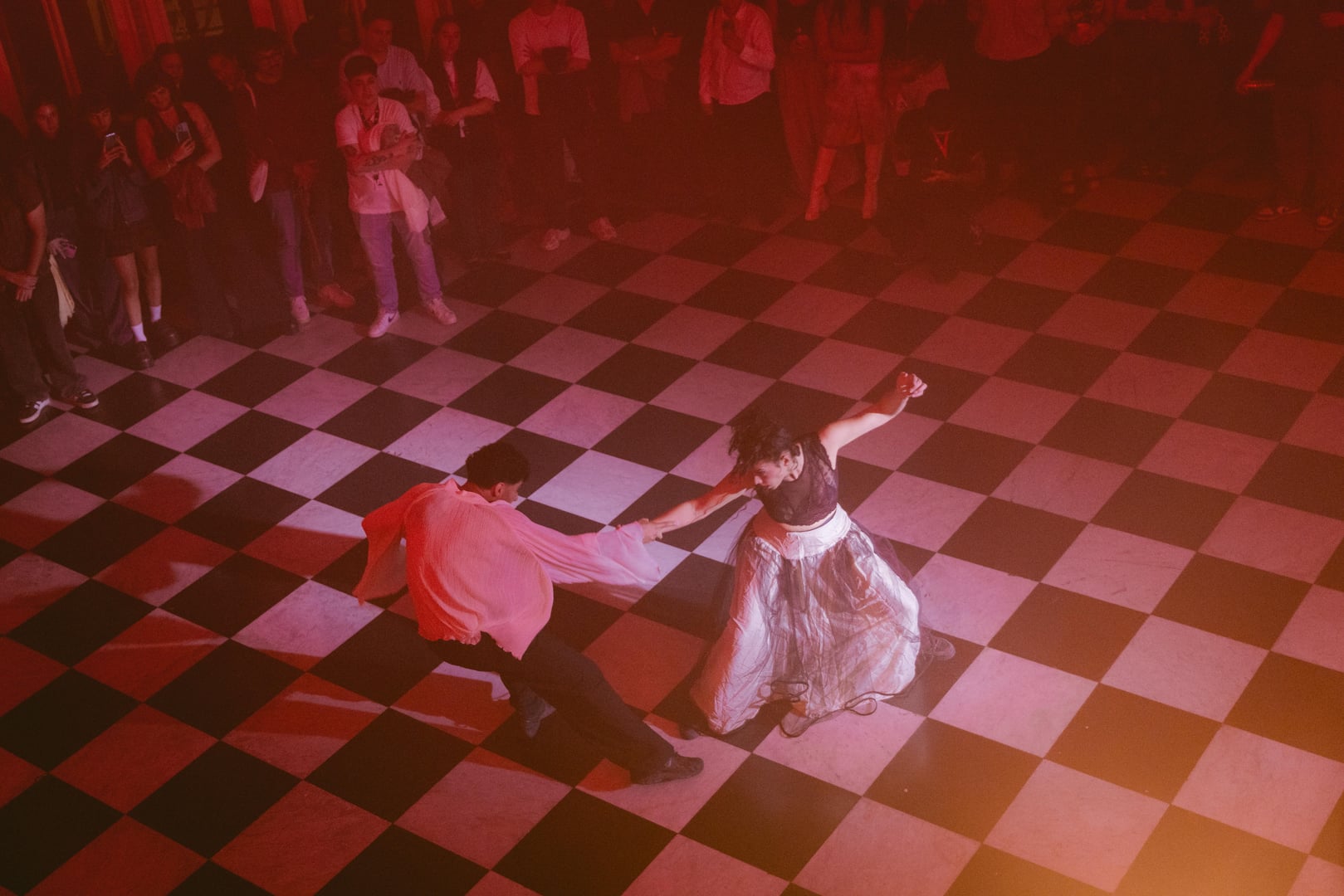 Dúo de bailarines sobre el piso ajedrezado bajo luz roja